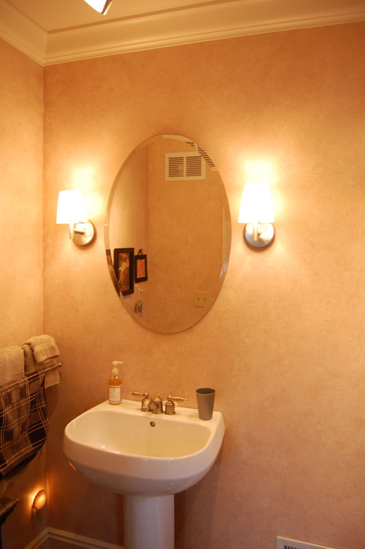 Oval mirror over sink with large light fixtures on either side.
