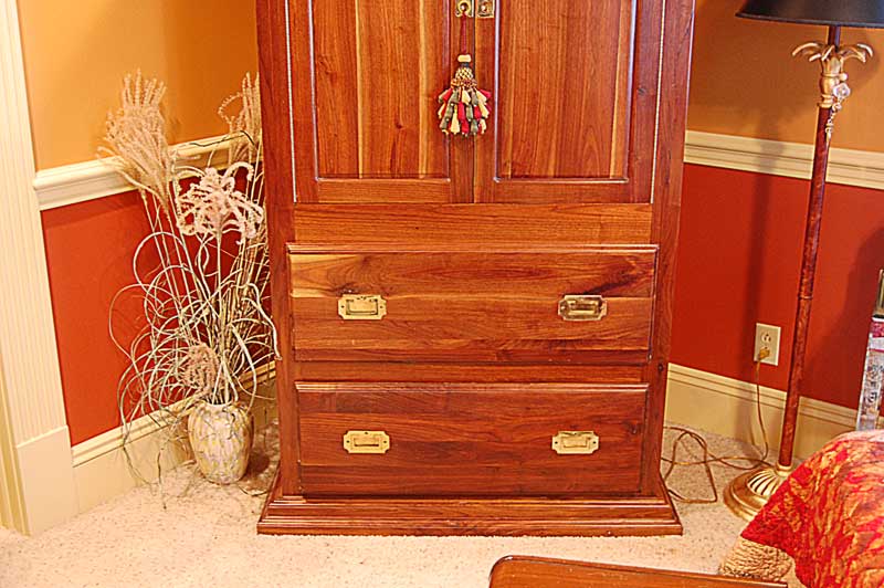 MId-tone wood armoire with 2 wide drawers at bottom and 2 long doors at top, with ornate gold fixtures zoom in on bottom drawers.